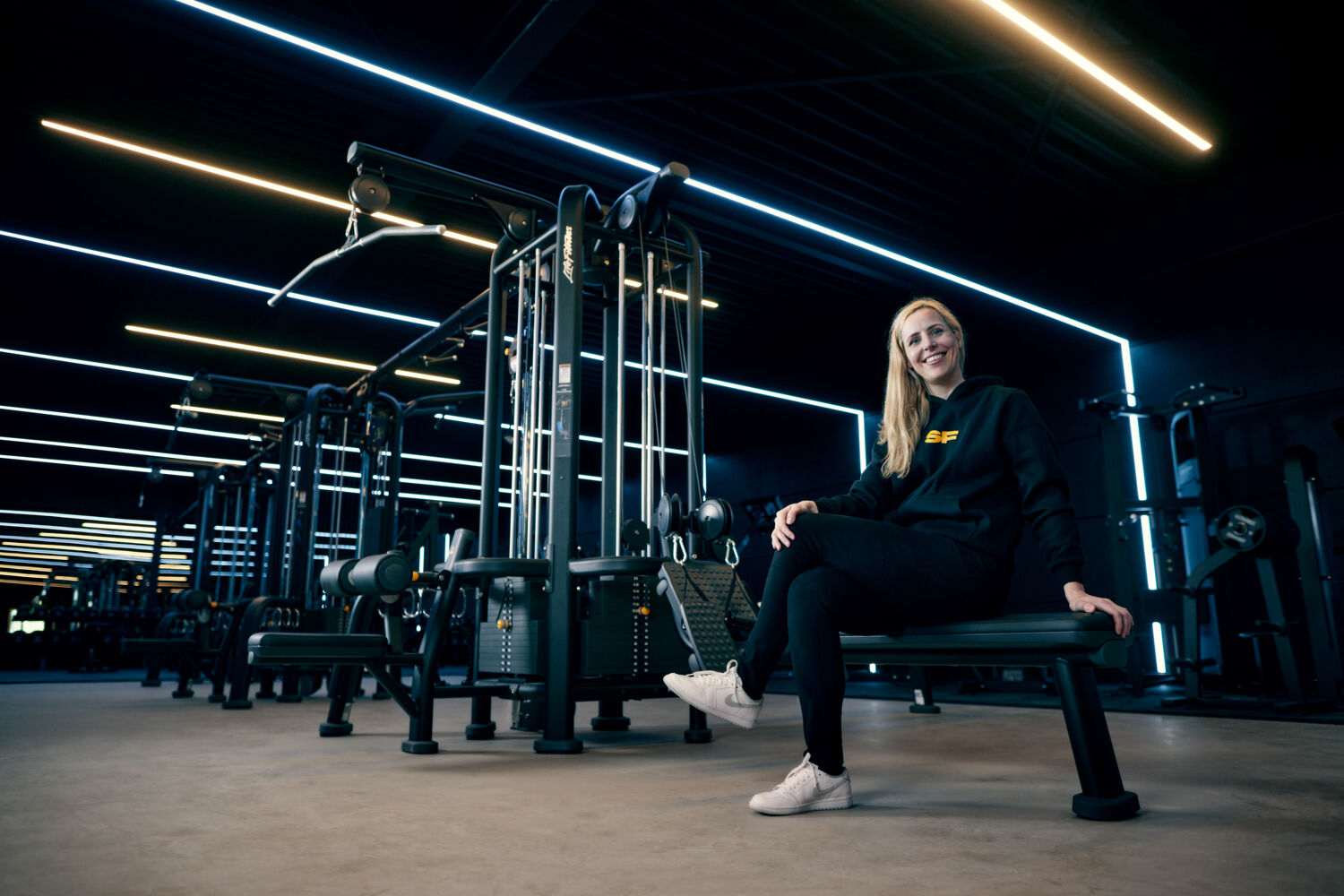 Vrouw zit lachend op een sportbankje in de sportschool.