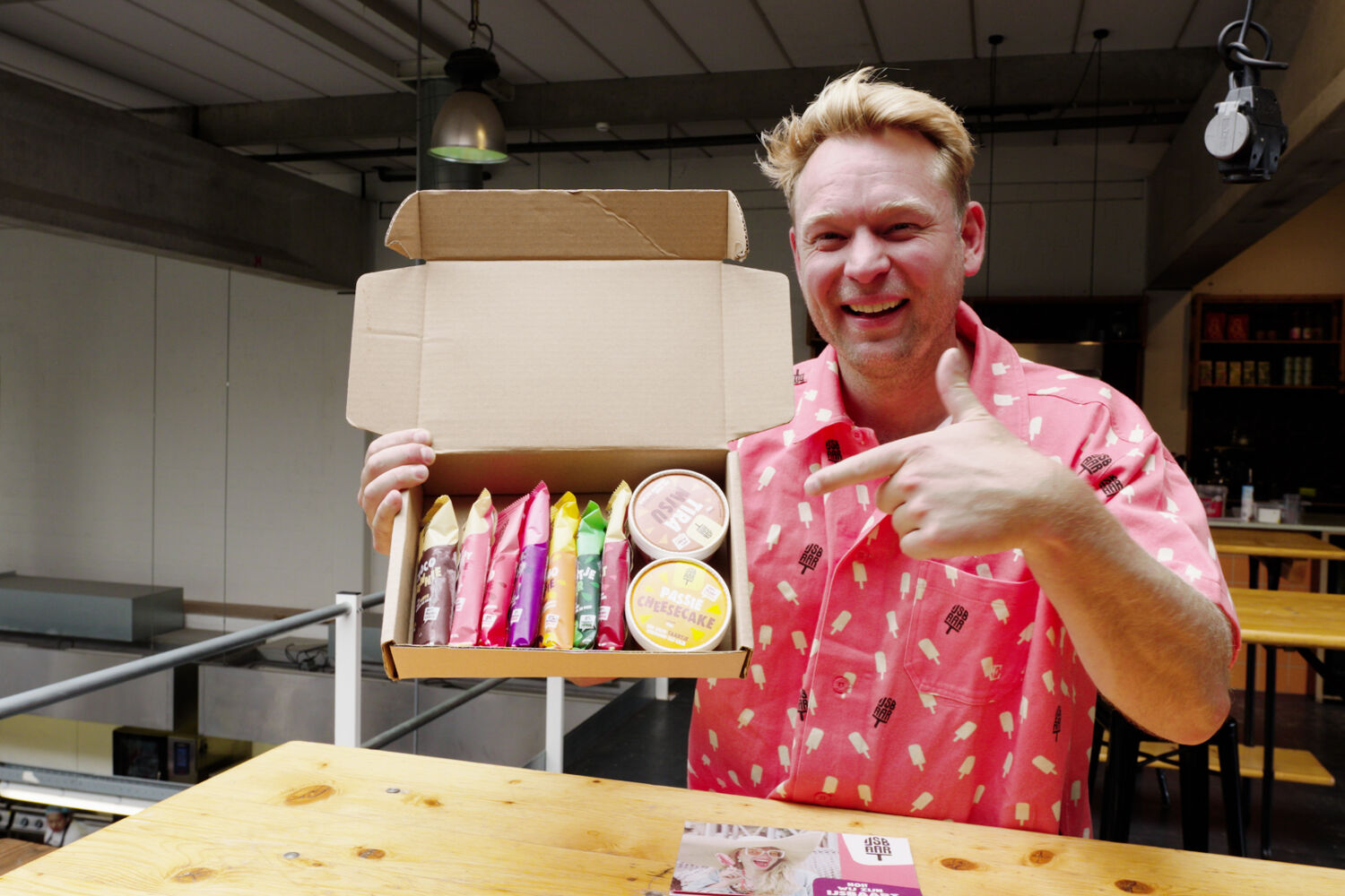 Lachende man in roze shirt houd een doos ijsjes vast en wijst ernaar