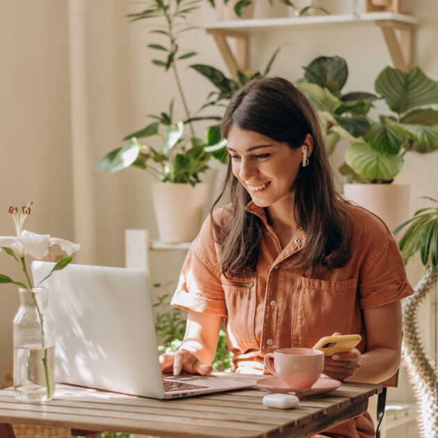 Vrouw zit achter de laptop en met telefoon met veel planten