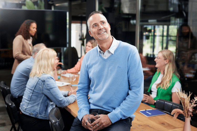 Man in blauw shirt zit op tafel en kijkt dromerig 