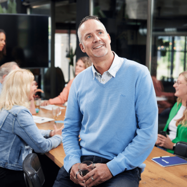 Man in blauw shirt zit op tafel en kijkt dromerig 