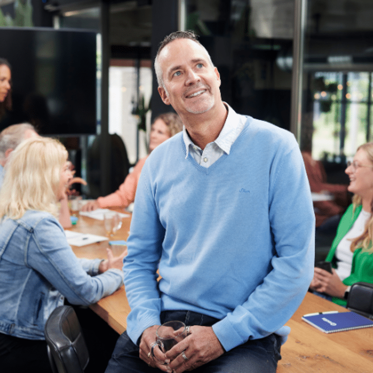Man in blauw shirt zit op tafel en kijkt dromerig 