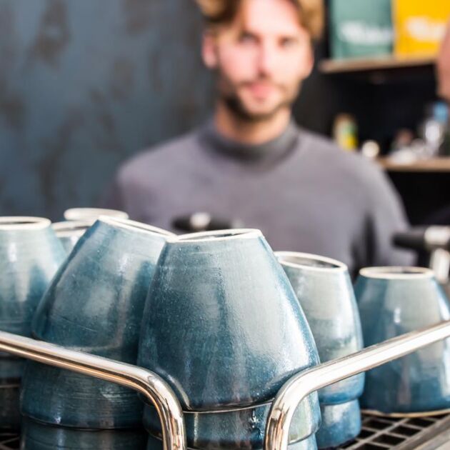 man in grijs shirt achter blauwe koffie kopjes