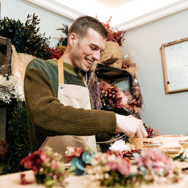 Een man is aan het lachen terwijl hij bloemen aan het schikken is. 