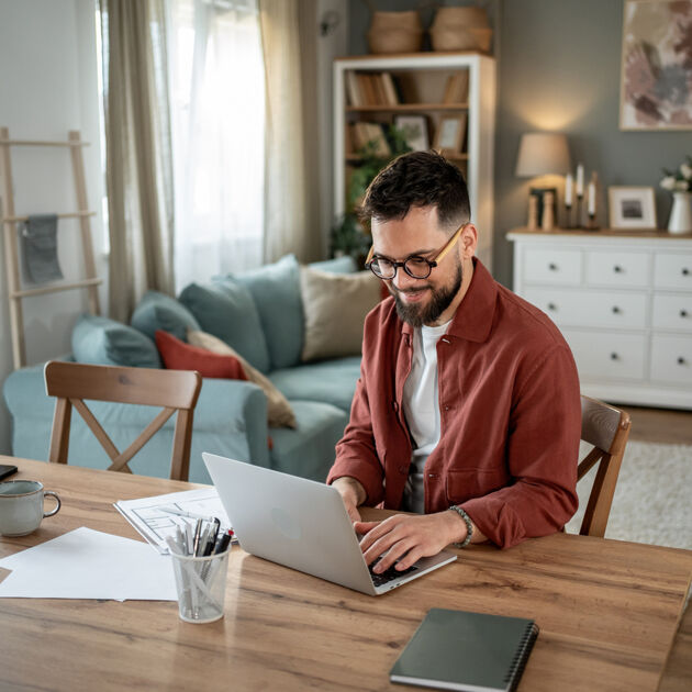 Een man met een bril zit aan een tafel en typt op zijn laptop.