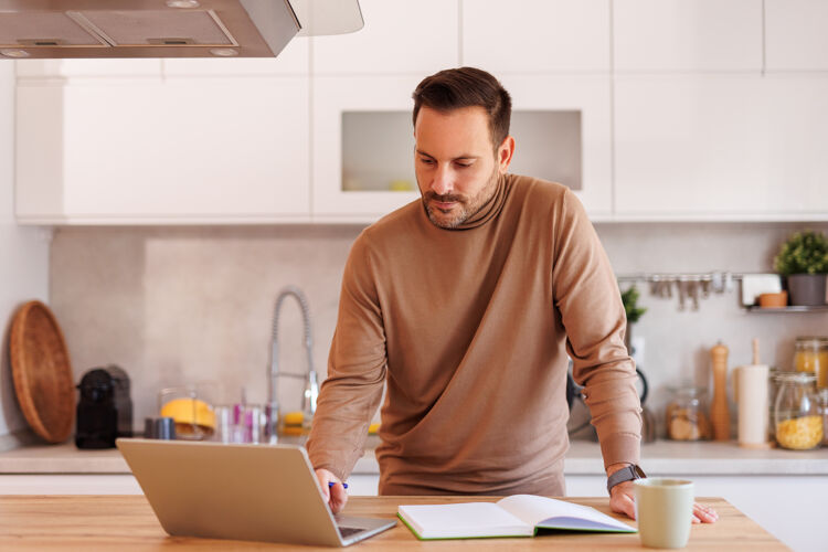 man-staat-aan-aanrecht-kijkt-naar-laptop