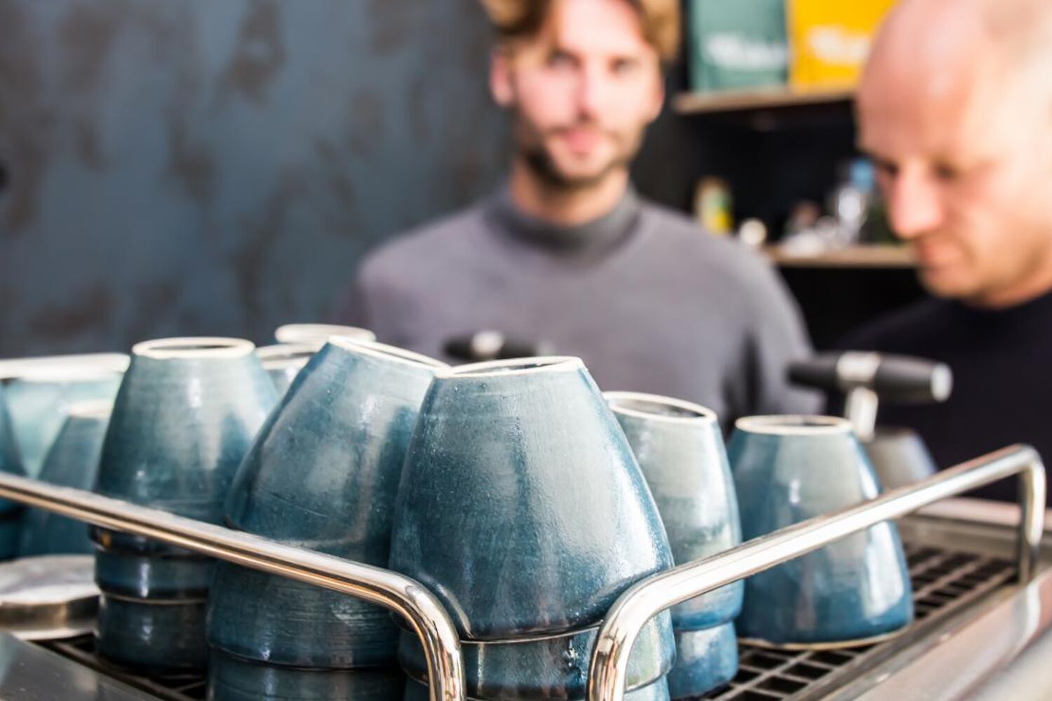 man in grijs shirt achter blauwe koffie kopjes