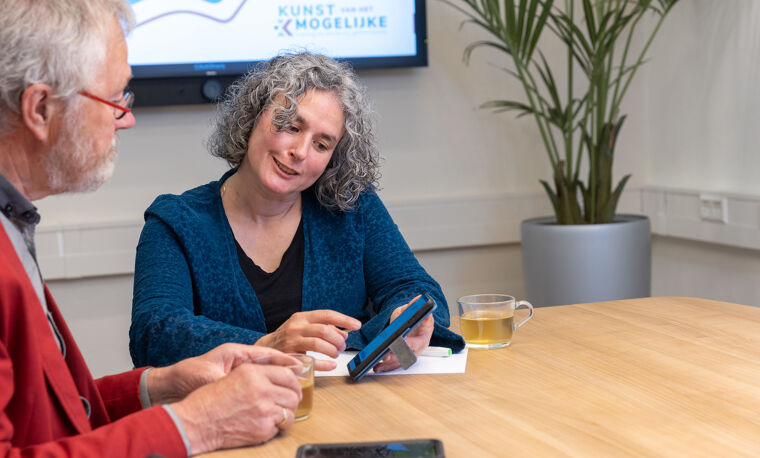 Vrouw in blauw shirt laat iets zien op telefoon aan man in rood
