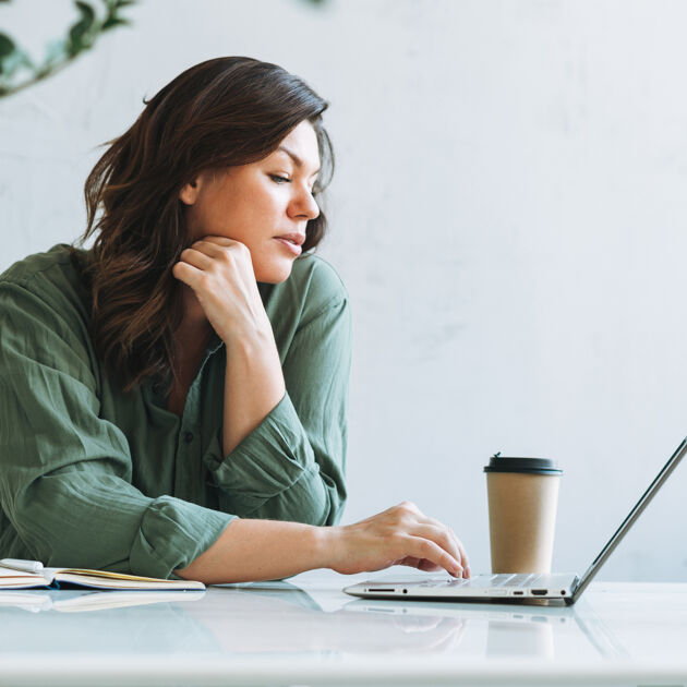 Vrouw met donker haar en groene blouse is bezig op laptop. 