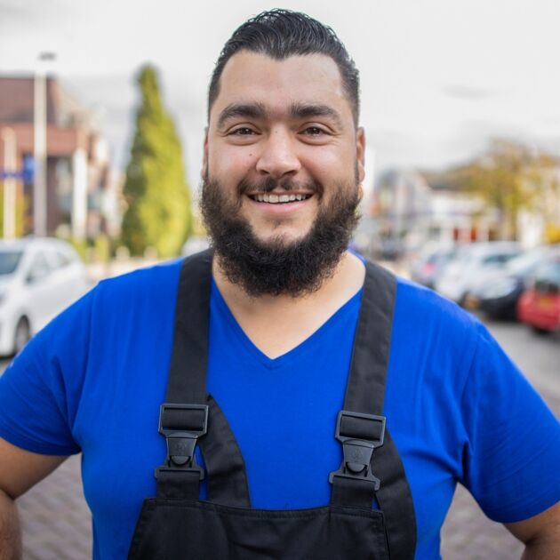 Man in blauw shirt lach naar de camera buiten 