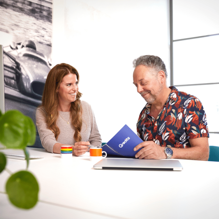 Vrouw praat met man aan tafel. Er is een laptop en Qredits boekje
