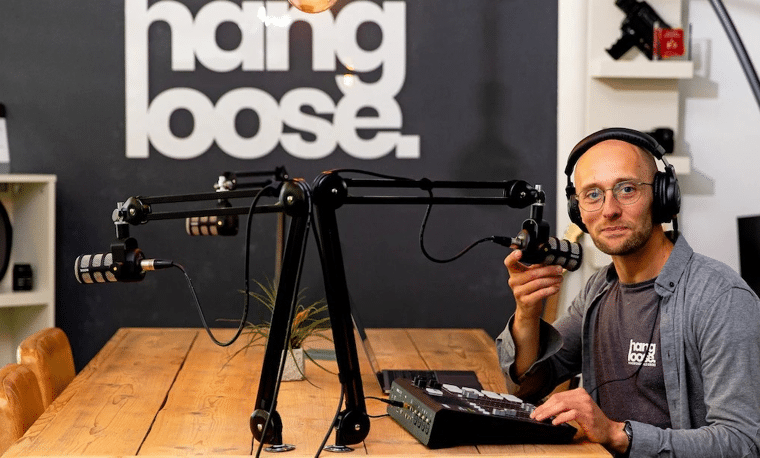 Kale man zit achter een tafel met een microfoon en hoofdtelefoons.