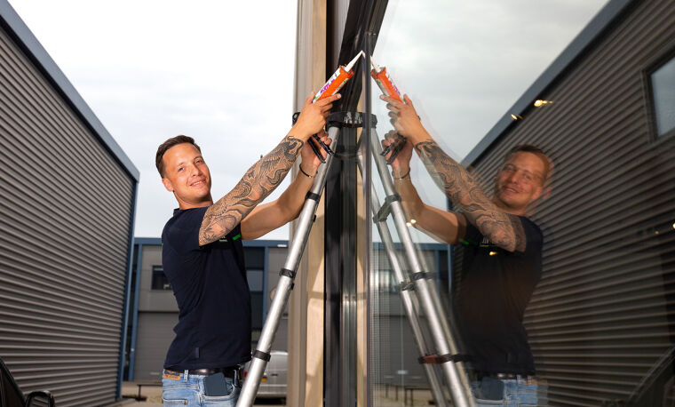 Man staat op een ladder en kit een raamkozijn 