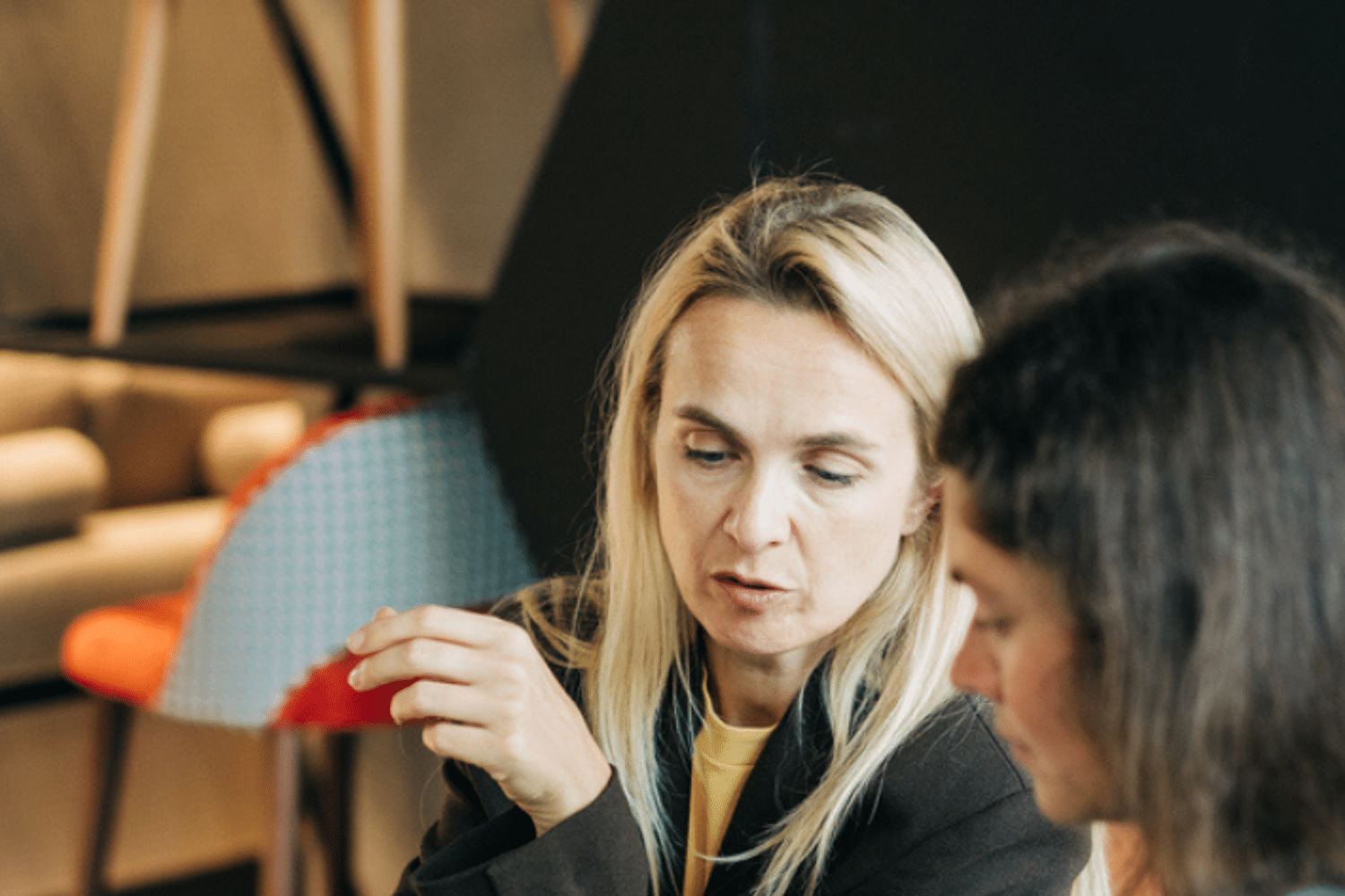 Twee vrouwen zitten aan tafel. Een vrouw legt iets uit aan de andere vrouw. 