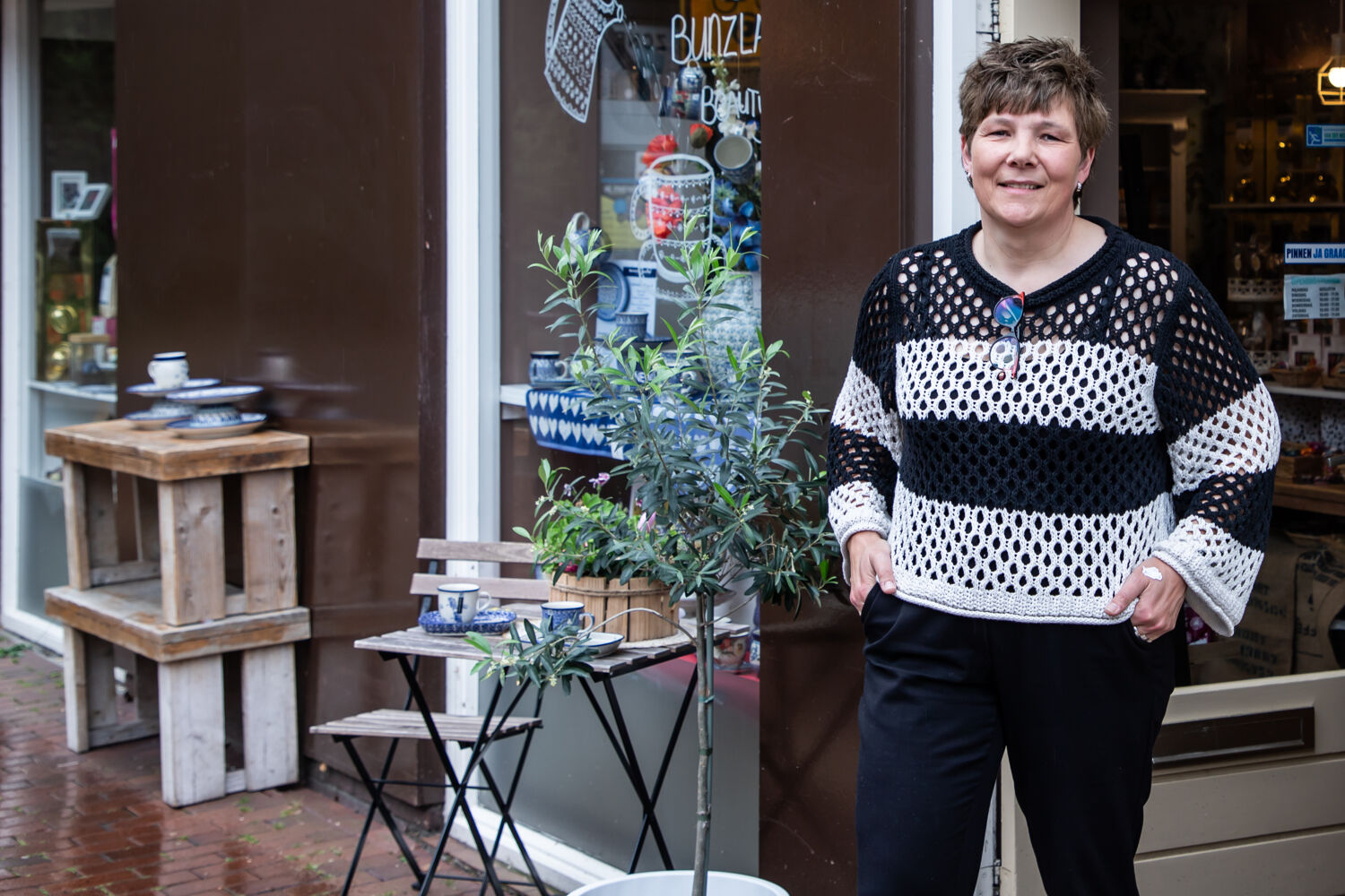 Vrouw in wit zwart shirt staat voor bedrijf met klein boompje