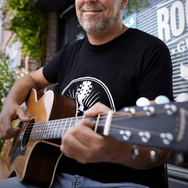 Man met zwart shirt en zonnebril speelt de gitaar buiten