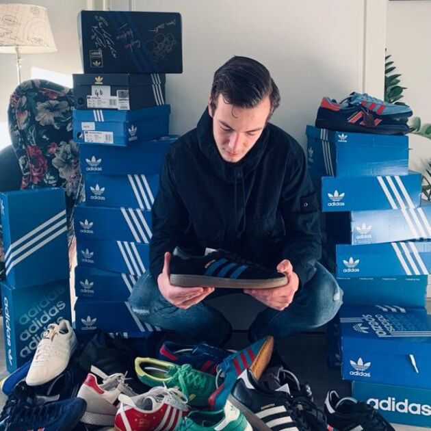 Een jongen heeft een berg schoenen voor zich liggen, achter hem staan veel blauwe schoenendozen.