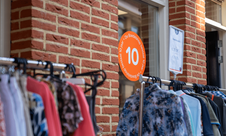 Zijkant bakstenen gebouw met oranje stikker op raam en kleding aan hangers