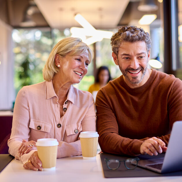 Man en vrouw zitten met een beker voor hun en kijken naar laptop.