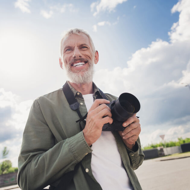 man lacht met camera in zijn handen met blauwe lucht op de achtergrond