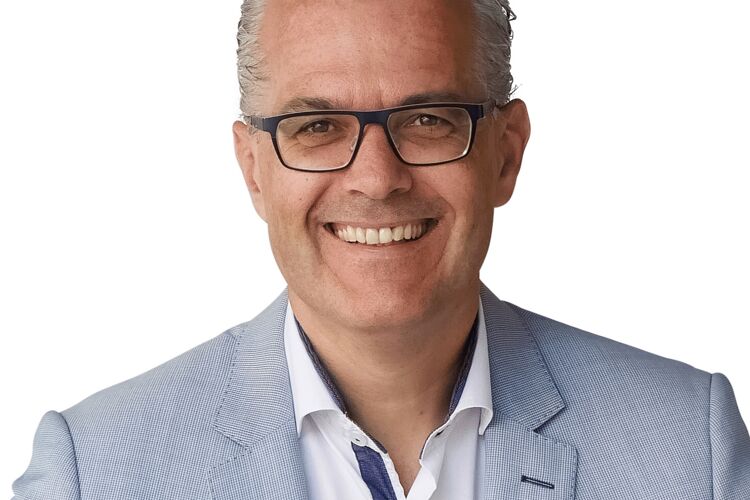 man met een bril op in lichtgrijs pak lacht