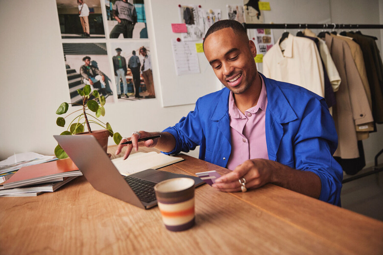 Man in blauw jasje en roze blouse werkt op zijn laptop aan een houten tafel