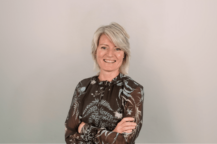 medewerker Qredits Sylvia van den Heerik vrouw in gebloemde blouse voor grijze achtergrond