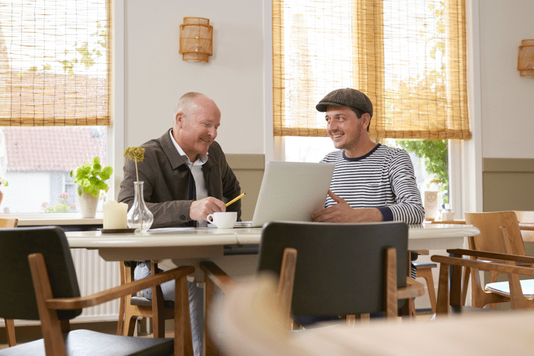 Twee mannen zitten aan tafel en praten met computer voor hun