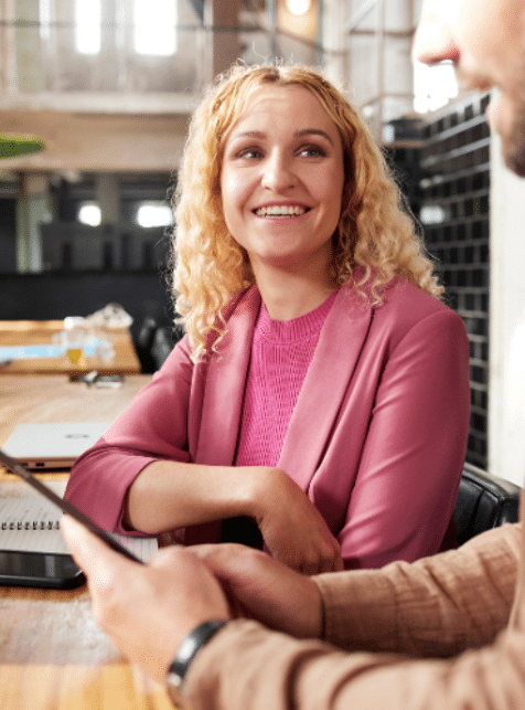 Vrouw in roze shirt en jasje kijkt naar man in bruin shirt die iets uitlegt