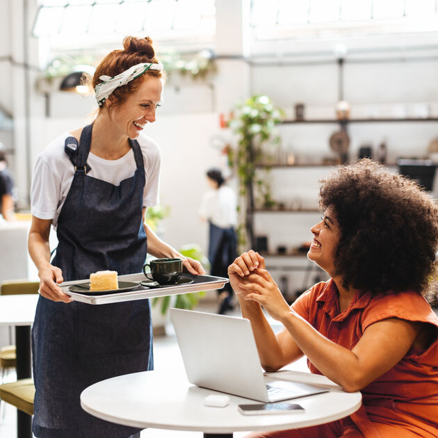 Vrouw met schort brengt vrouw koffie en cake