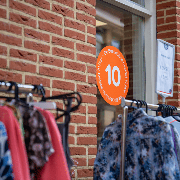 Zijkant bakstenen gebouw met oranje stikker op raam en kleding aan hangers
