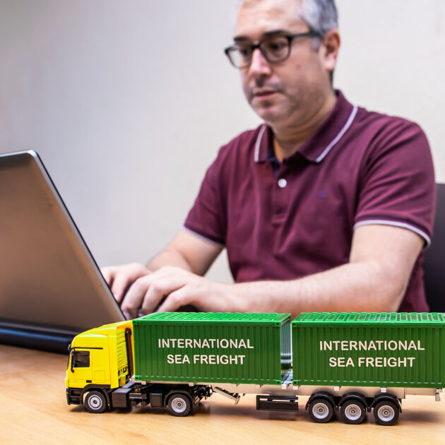 Man werkt achter zijn laptop.  Voor zijn laptop staat een miniatuur vrachtwagen.