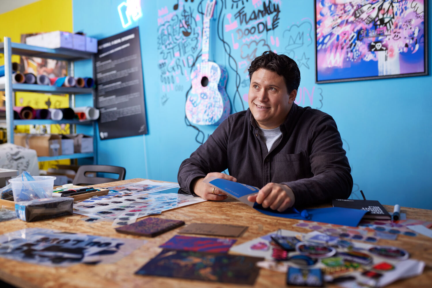 Lachende man zit aan een tafel voor een blauwe muur. 