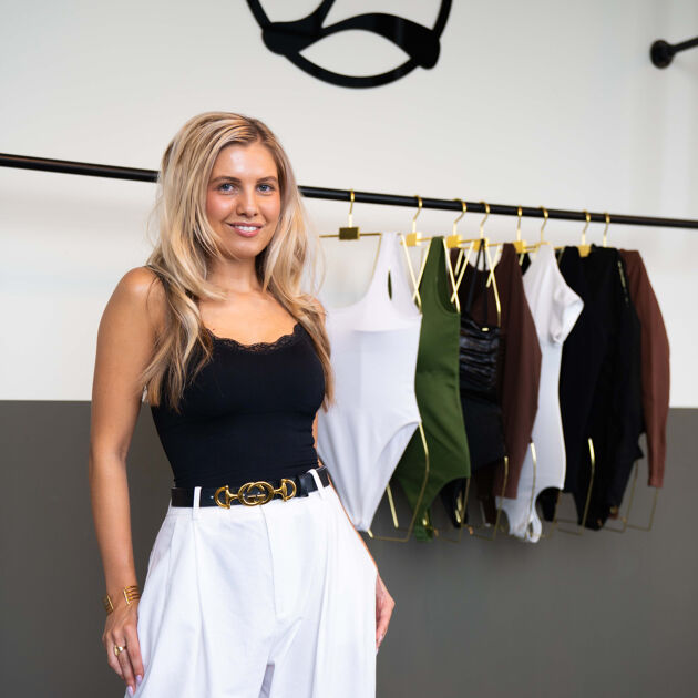 Vrouw met blonde haren staat voor rek met kleding.