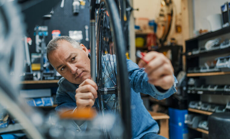 Man  in blauw shirt is bezig met een fietswiel repareren
