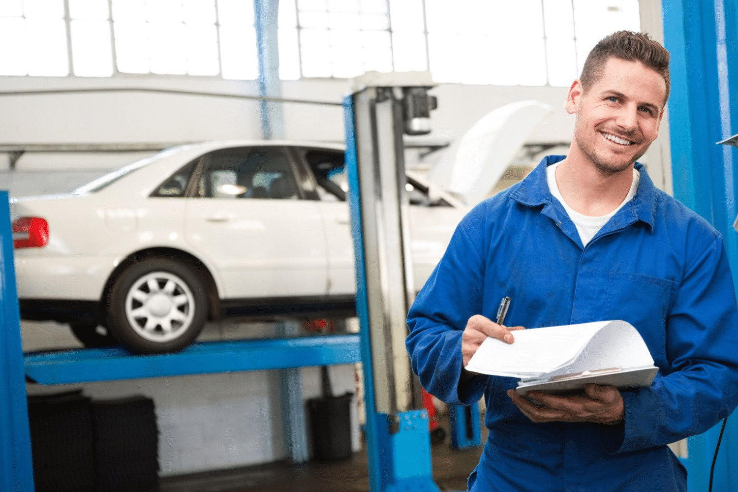 Man met blauwe overal staat naast auto en kijkt lachend.  