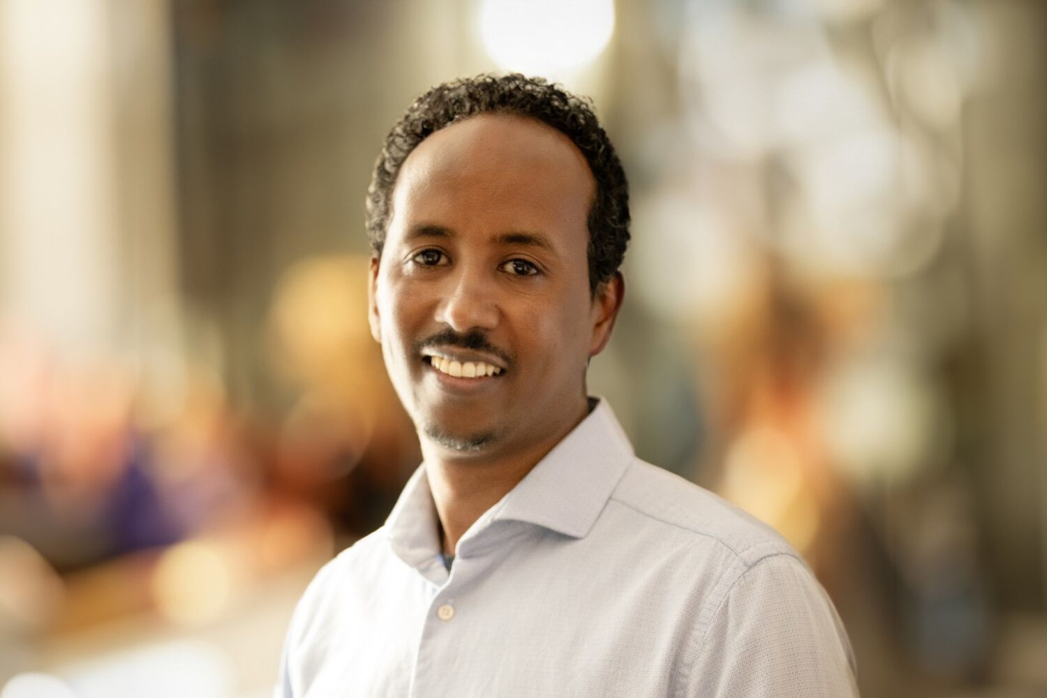 Man in witte blouse lacht naar de camera met wazige achtergrond Man in witte blouse lacht naar de camera met wazige achtergrond