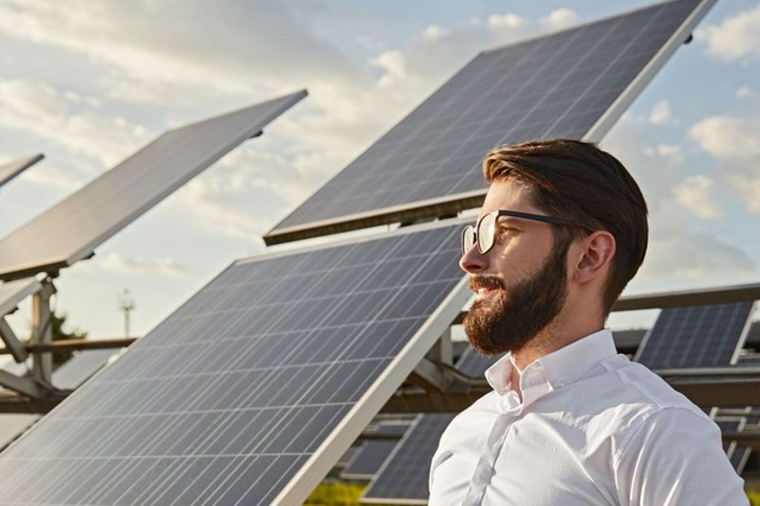 man-met-helm-naast-zonnepaneel-header Man met bril op en witte blouse staat met helm in de handen naast zonnepaneel.