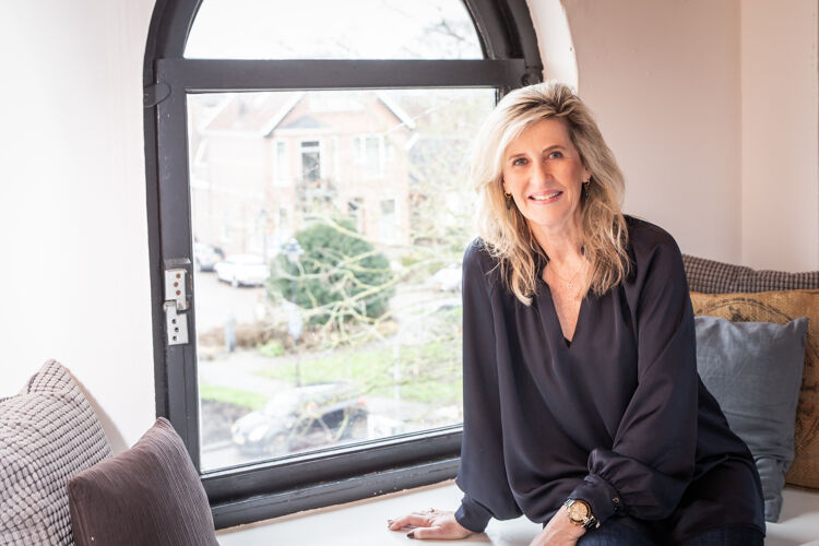 Vrouw met zwarte blouse, zit lachend voor een raam.