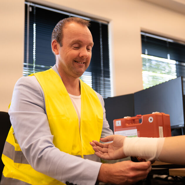 Lachende man met geel hesje rolt verband om pols.