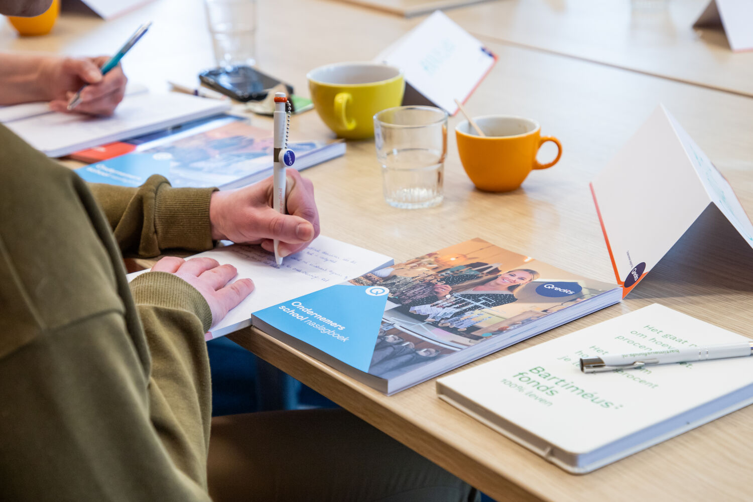 Houten tafel met kopjes en boeken van Qredits er word geschreven
