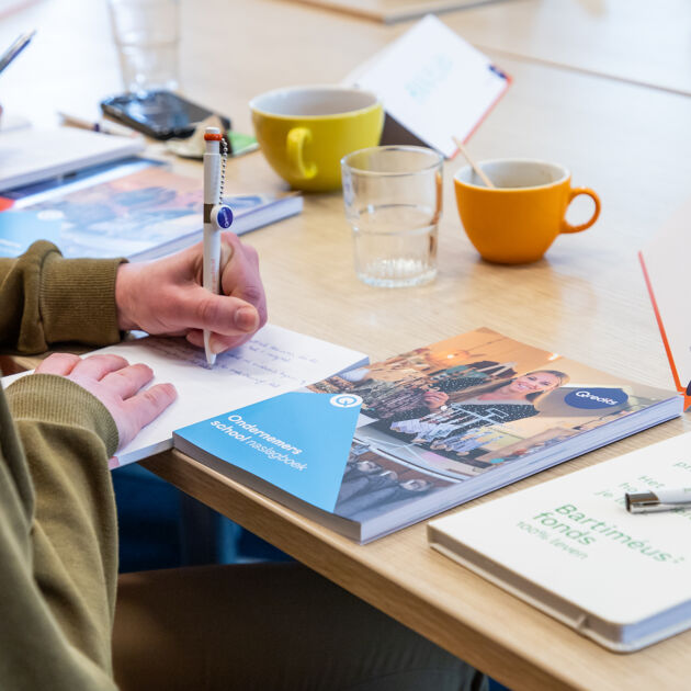 Houten tafel met kopjes en boeken van Qredits er word geschreven