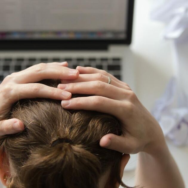 Vrouw zit met handen in het haar bij haar laptop.