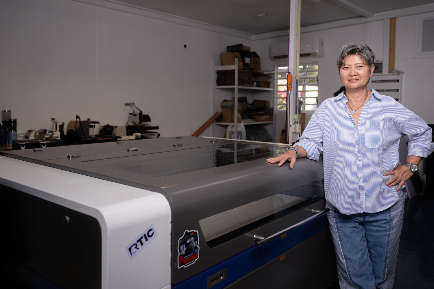 Vrouw leunt tegen een machine en kijkt in de camera. Donkere ruimte.