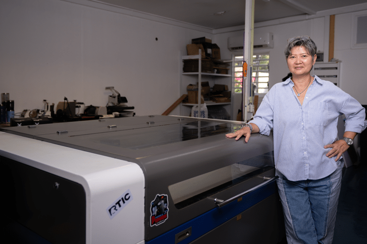 Vrouw leunt tegen een machine en kijkt in de camera. Donkere ruimte.