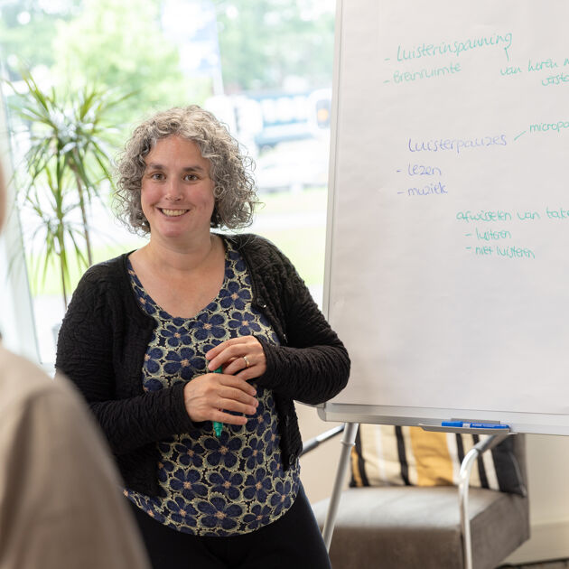 Vrouw in bloemen shirt staat voor een whiteboard