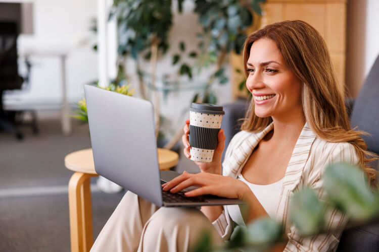 vrouw-kijkt-lachend-naar-laptop-koffiebeker-in-hand