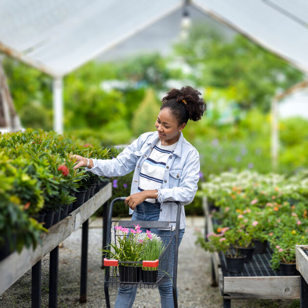Vrouw leunt op een karretje en kijkt naar planten. 