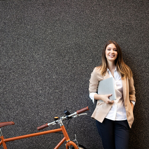 Vrouw heeft een map in haar handen en staat met haar fiets tegen een muur