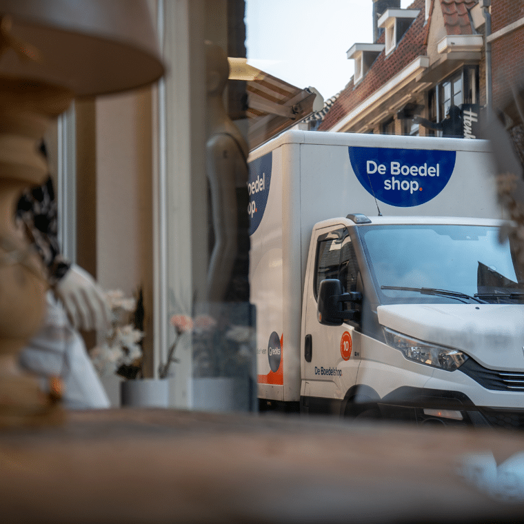 Wit busje van De Boedel Shop als gezien door een raam